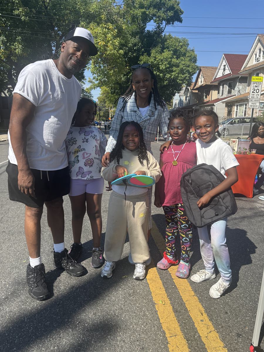 Lamont in a white t-shirt and cap with a group of kids in the closed street, one carrying a new backpack and another holding a paddle-ball set