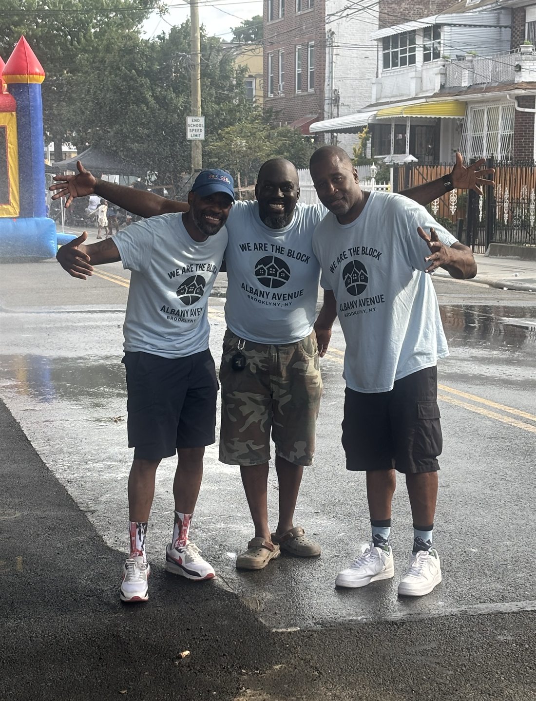 Prance, Donovan and Lamont in We Are The Block t-shirts, arms out, standing together in the middle of Albany Avenue at the 2026 block party
