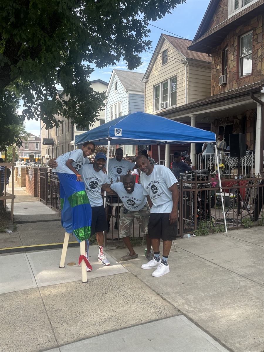Neighbors in We Are The Block t-shirts standing together under the tent on the sidewalk