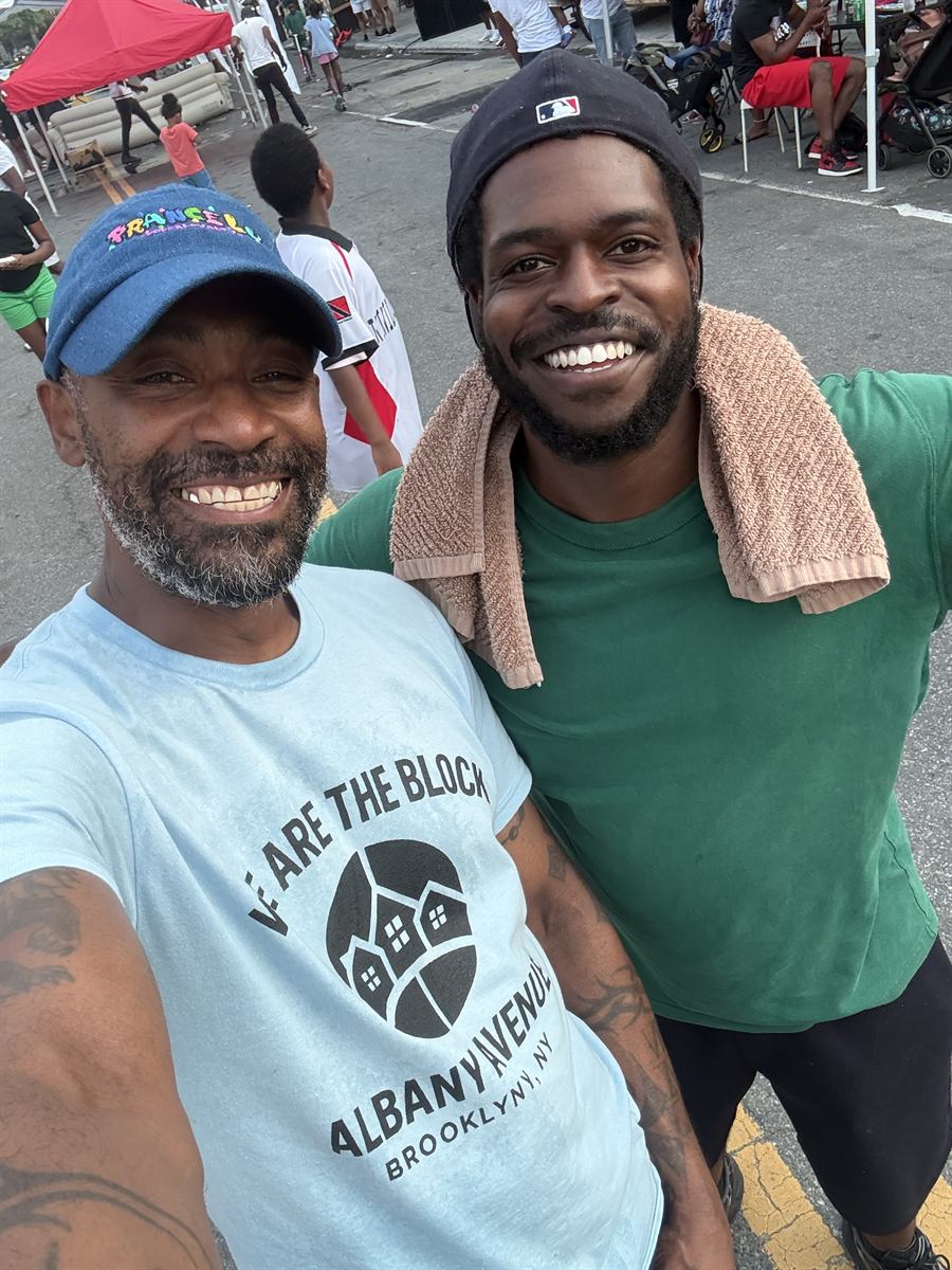 Two neighbors side by side out on the avenue, one in a We Are The Block t-shirt