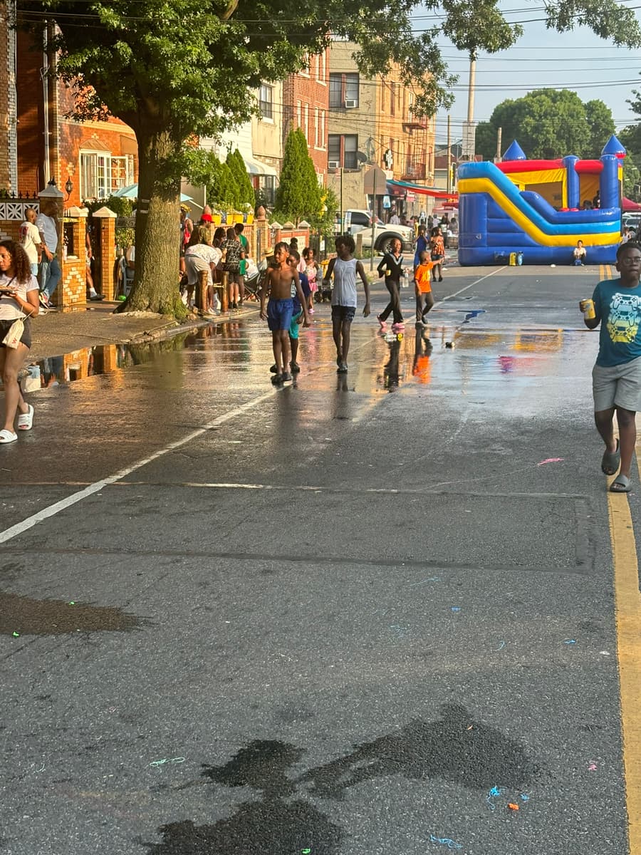 Looking down Albany Avenue, families walking the wet street past the bouncy houses