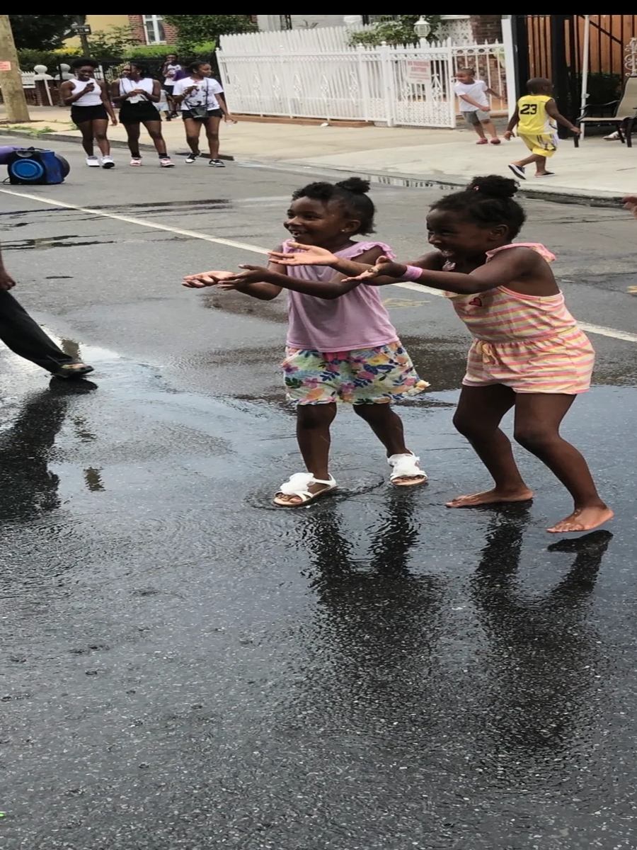 Two little girls dancing together in the middle of the wet street