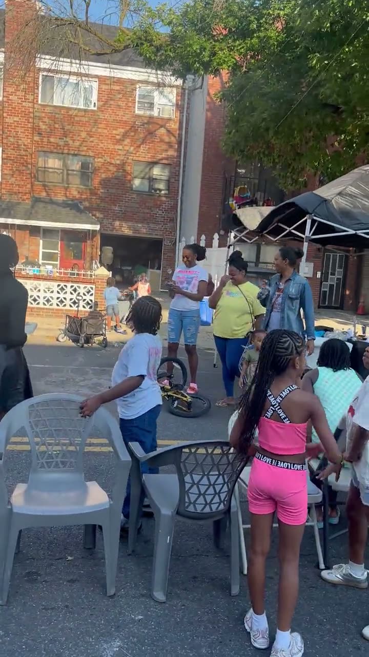 Kids circling a row of folding chairs set out in the middle of the street for musical chairs