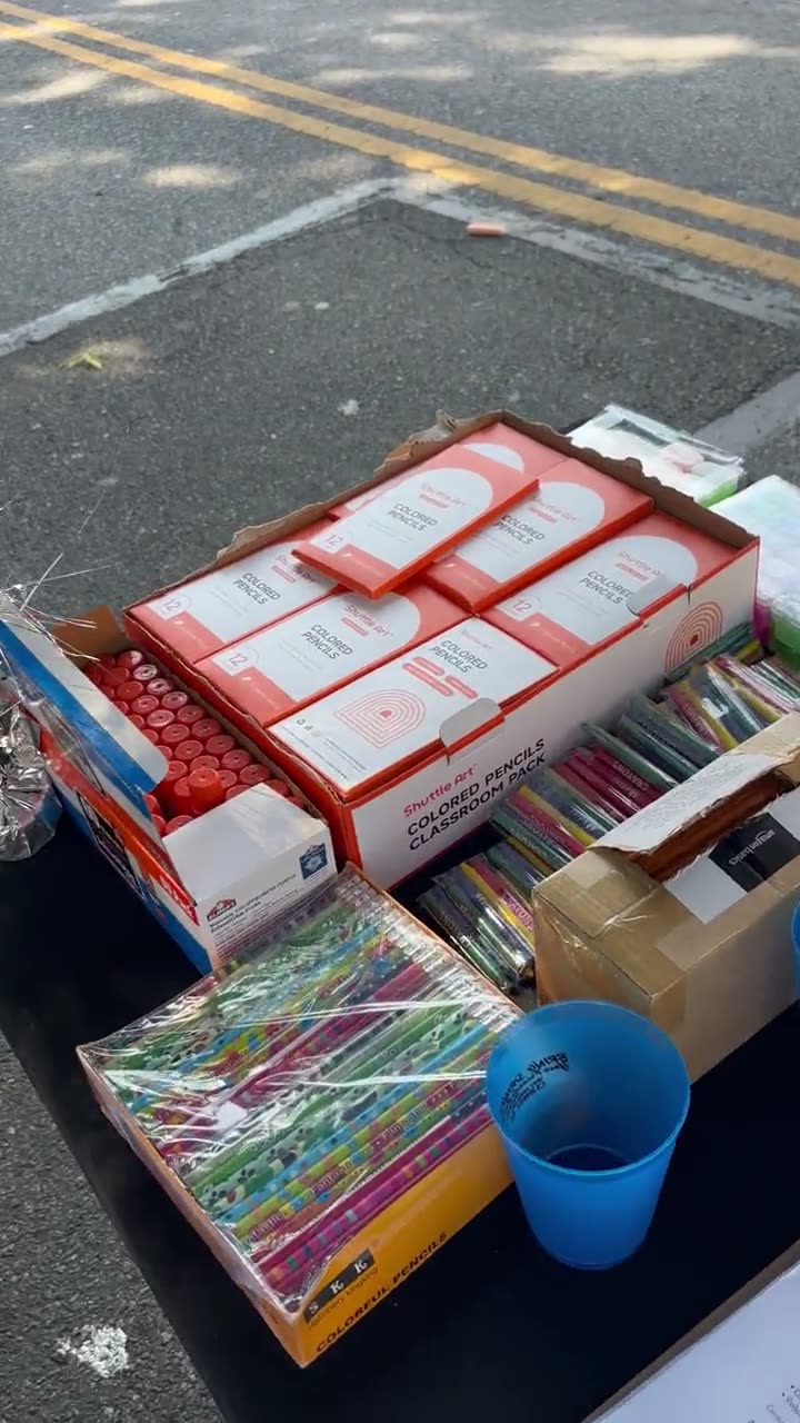 Boxes of crayons, markers, coloured pencils and notebooks laid out across the supply table in the street