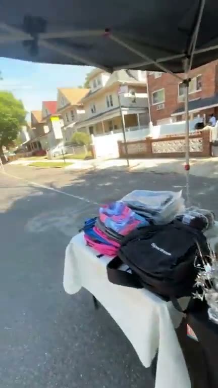 Lamont walking the closed block, past a table stacked with new backpacks under the canopy
