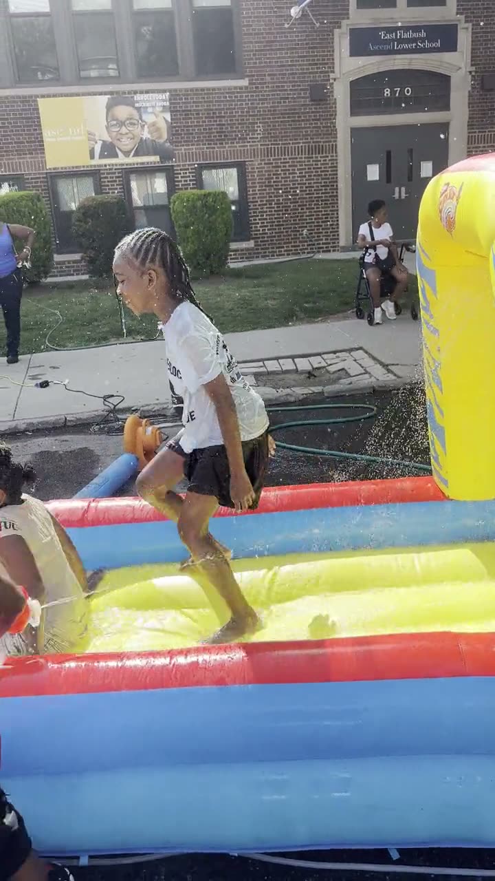 Kids running and sliding through the water on the inflatable water slide in the closed street